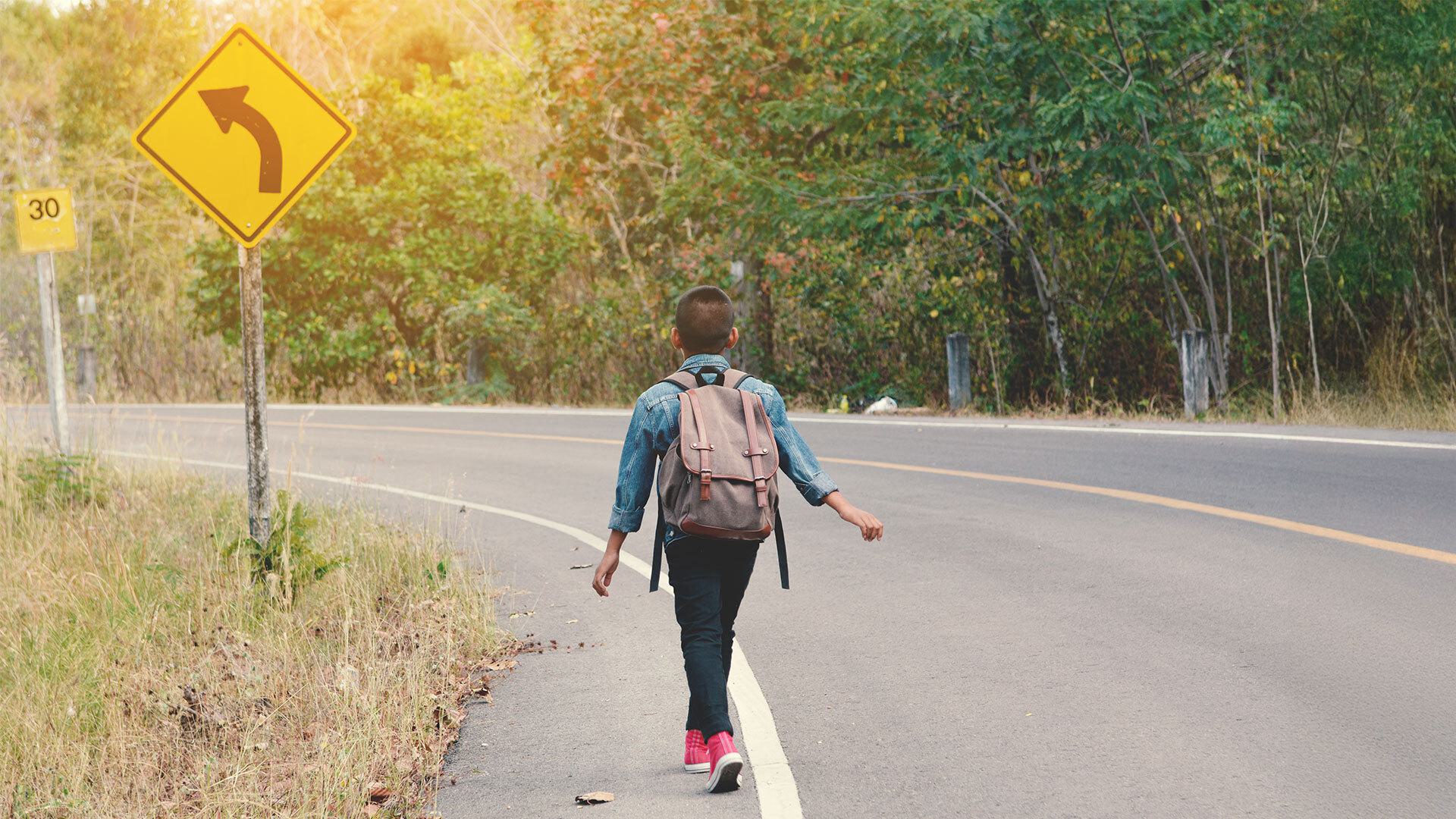 young student walks down street, with sign indicating curve to the left