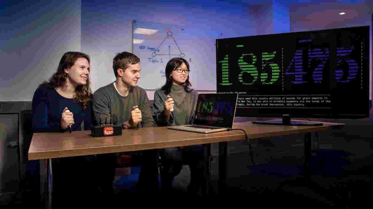 three students hold buzzers as they test AI question and answering machine