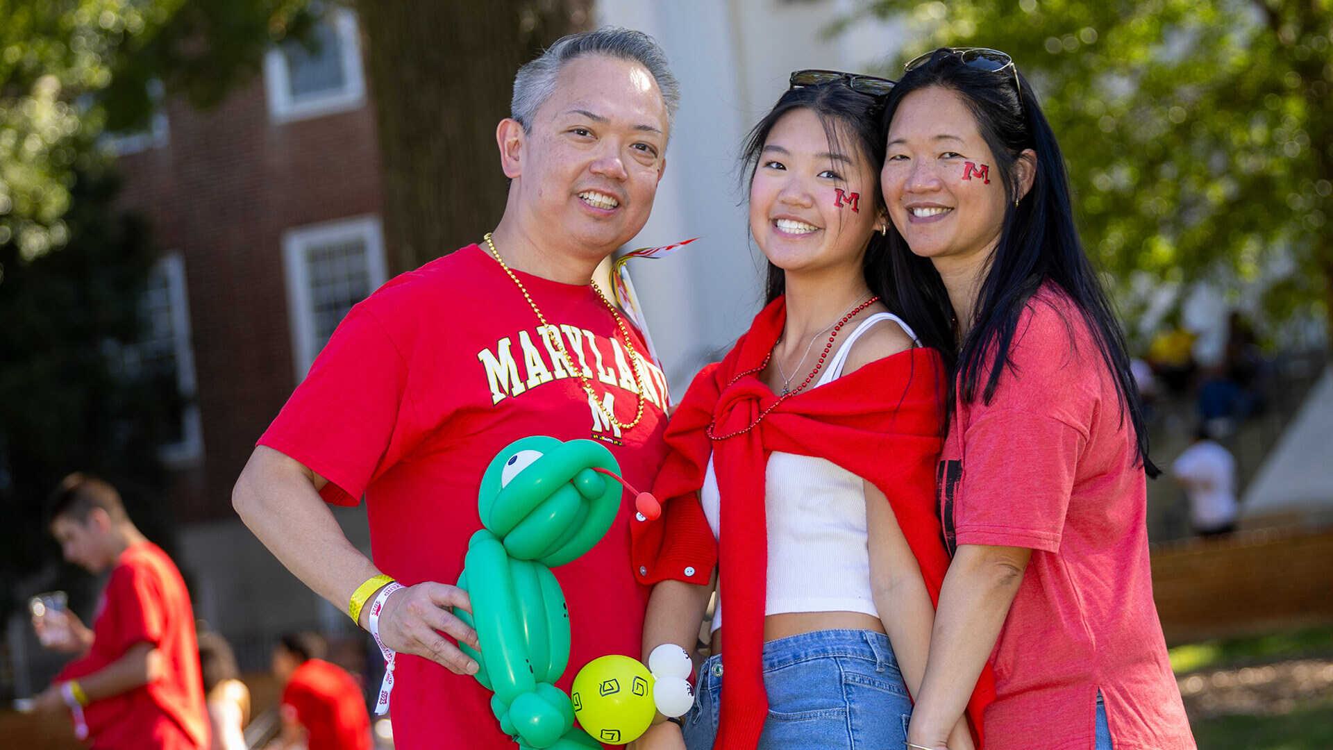 Two smiling parents and smiling daughter, all with M face paint and Terps gear, pose on McKeldin Mall