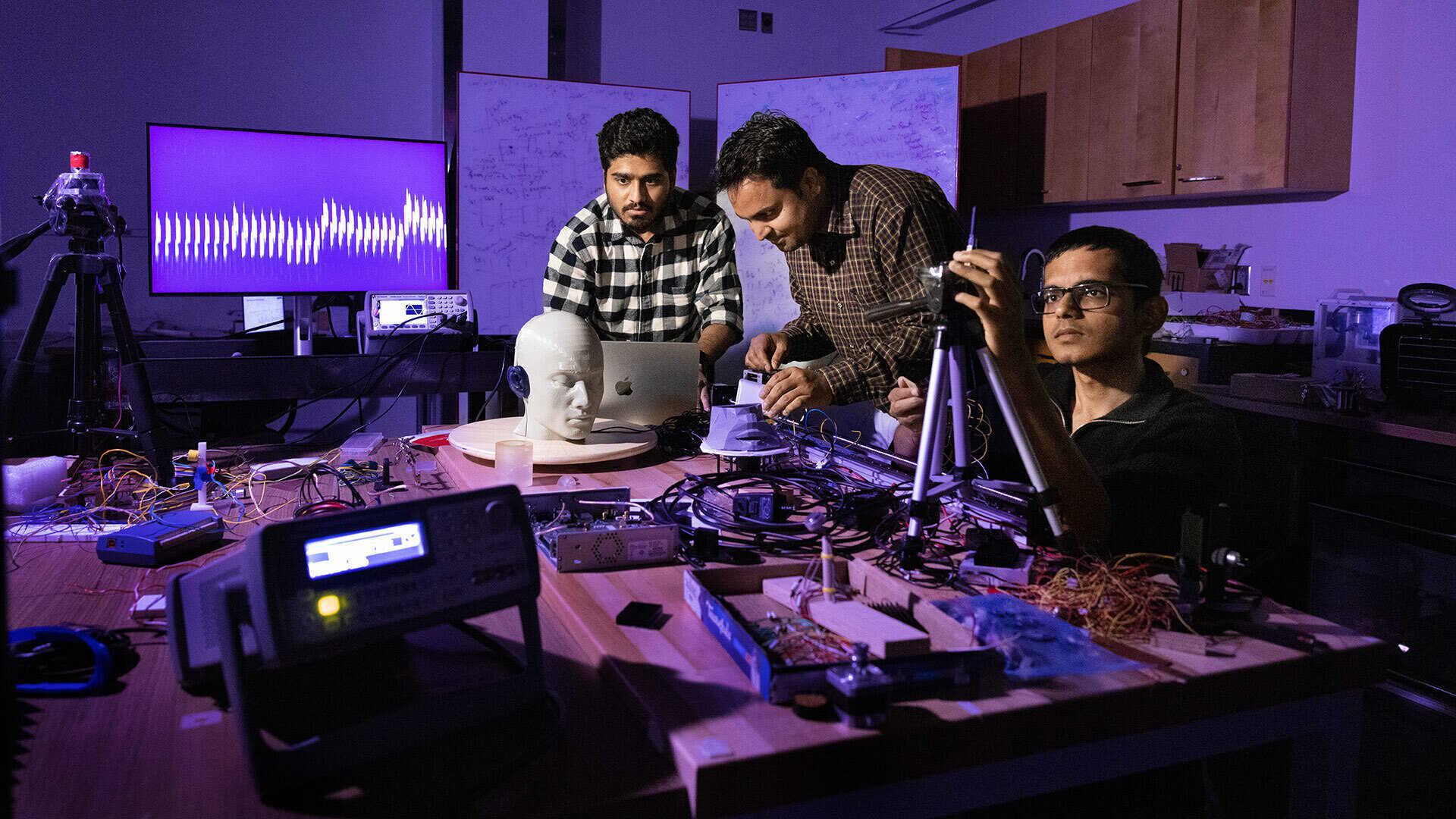 three researchers work in lab amid purple light