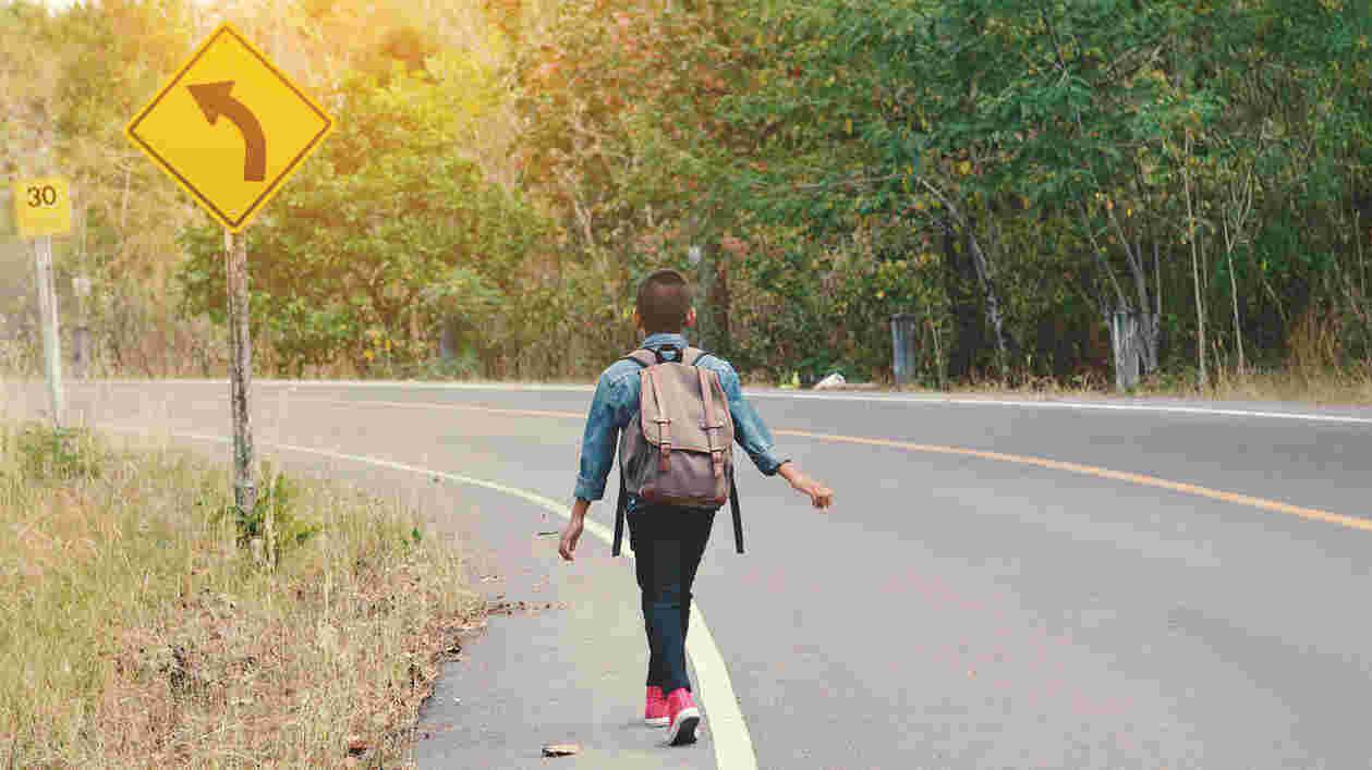 young student walks down street, with sign indicating curve to the left