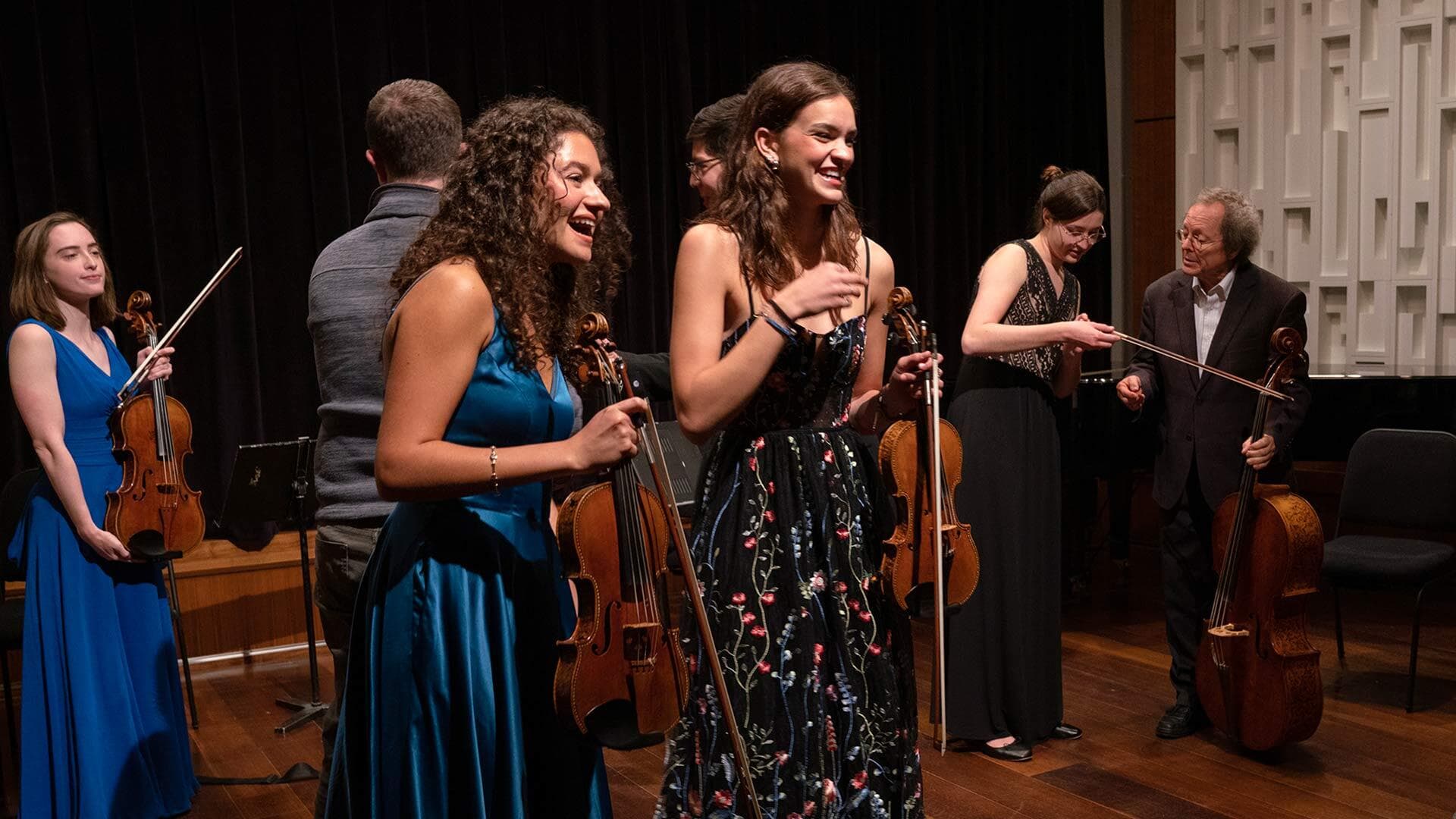 students hold violins on stage