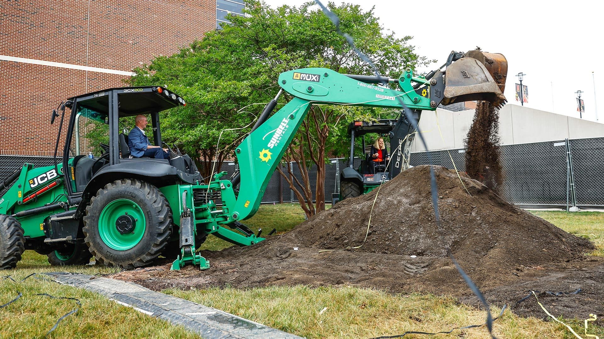 Kevin Willard and Brenda Frese scoop dirt with excavators