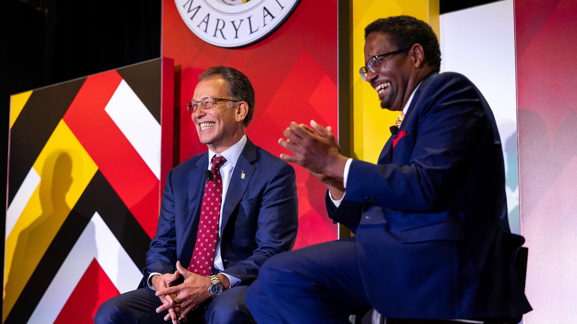 two men sit on stage and seem to engage with the audience
