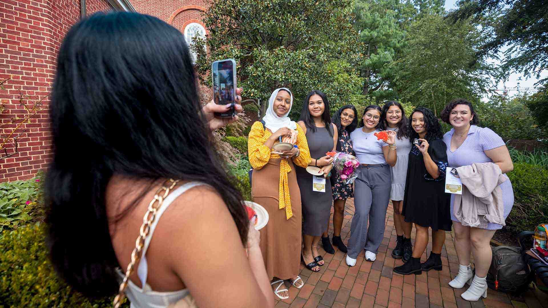 Student takes a photo of group of students smiling outdoors