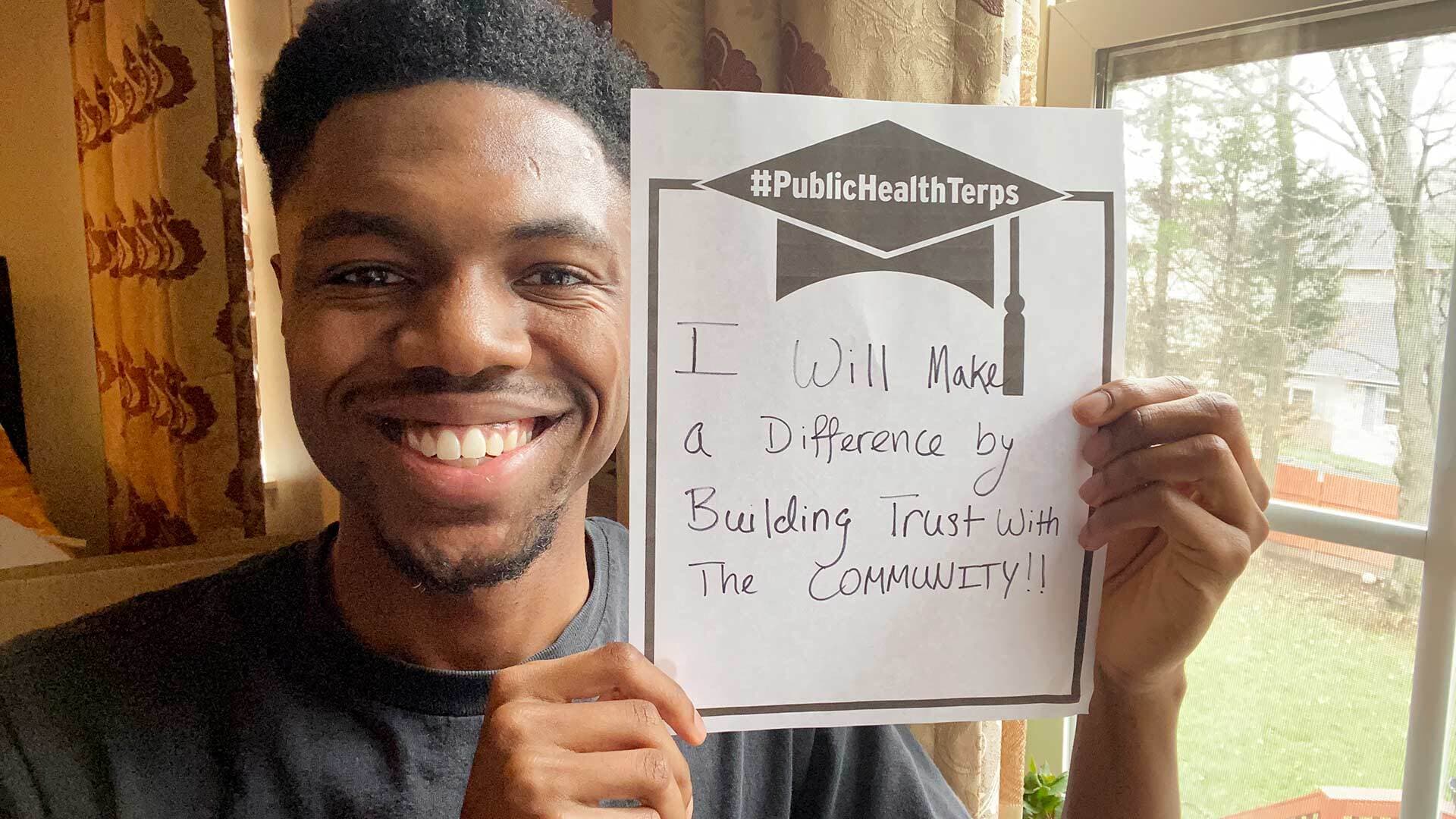 Student holding paper that reads: "#PublicHealthTerps: I will make a difference by building trust with the community!!"