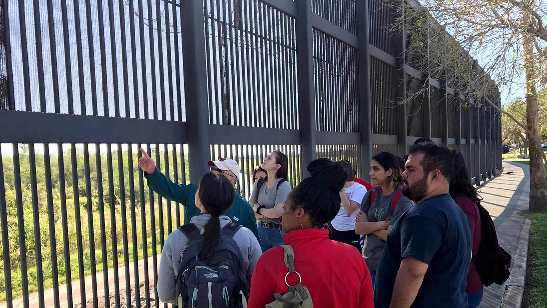 students stand near a fence separating the U.S. and Mexico
