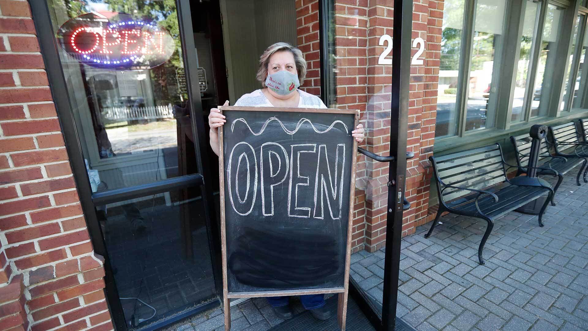 Woman wearing face mask and holding "Open" sign outside a restaurant