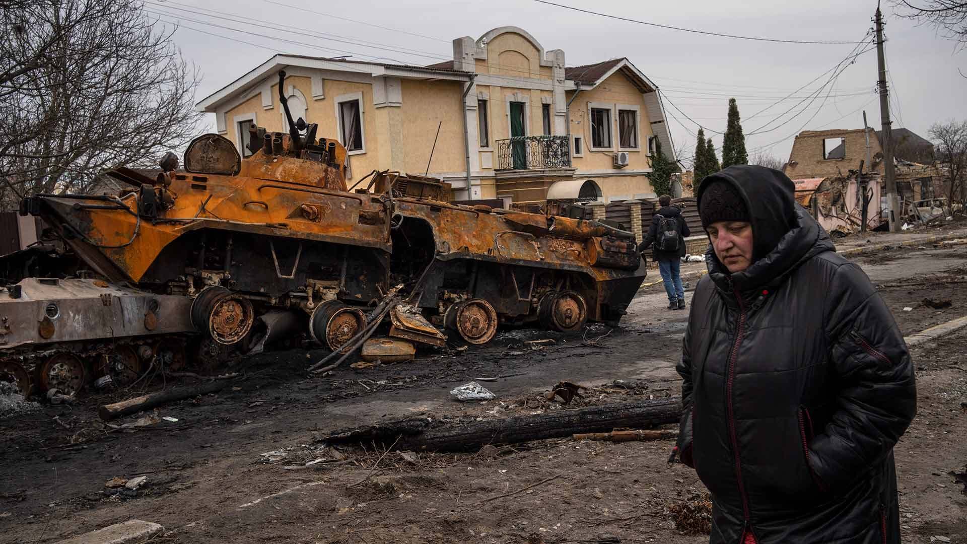 woman walks next to a destroyed Russian armor vehicle in Bucha