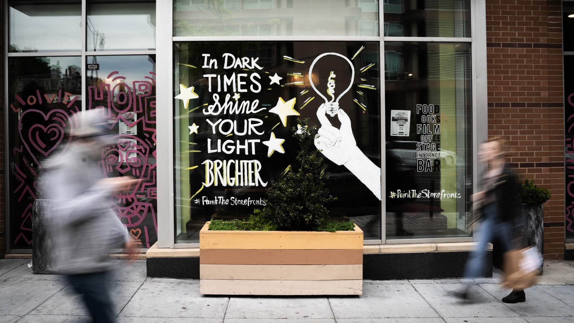 Window with “In Dark Times, Shine Your Light Brighter” painted on it
