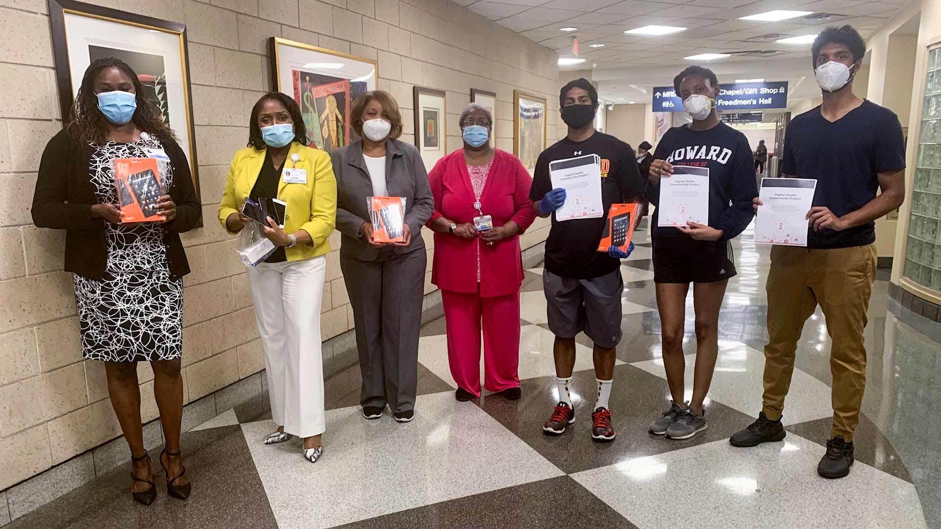 Seven people wearing masks hold up donated smart devices at Howard University Hospital