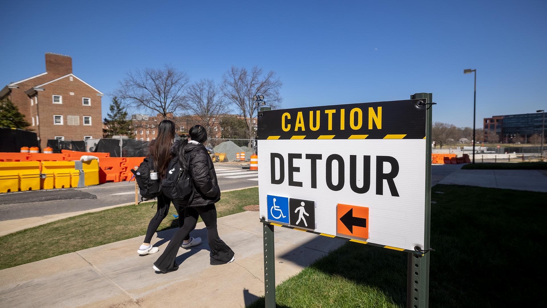 two students walk past "CAUTION: DETOUR" sign on campus