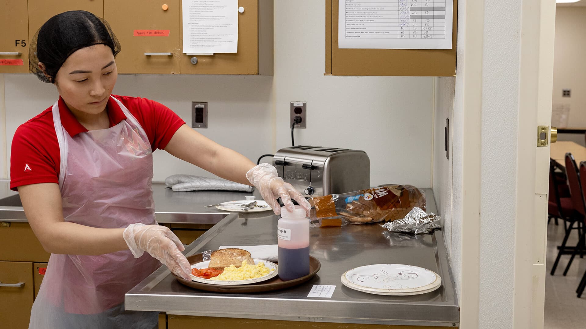 grad student wearing apron, hair net and gloves prepares breakfast
