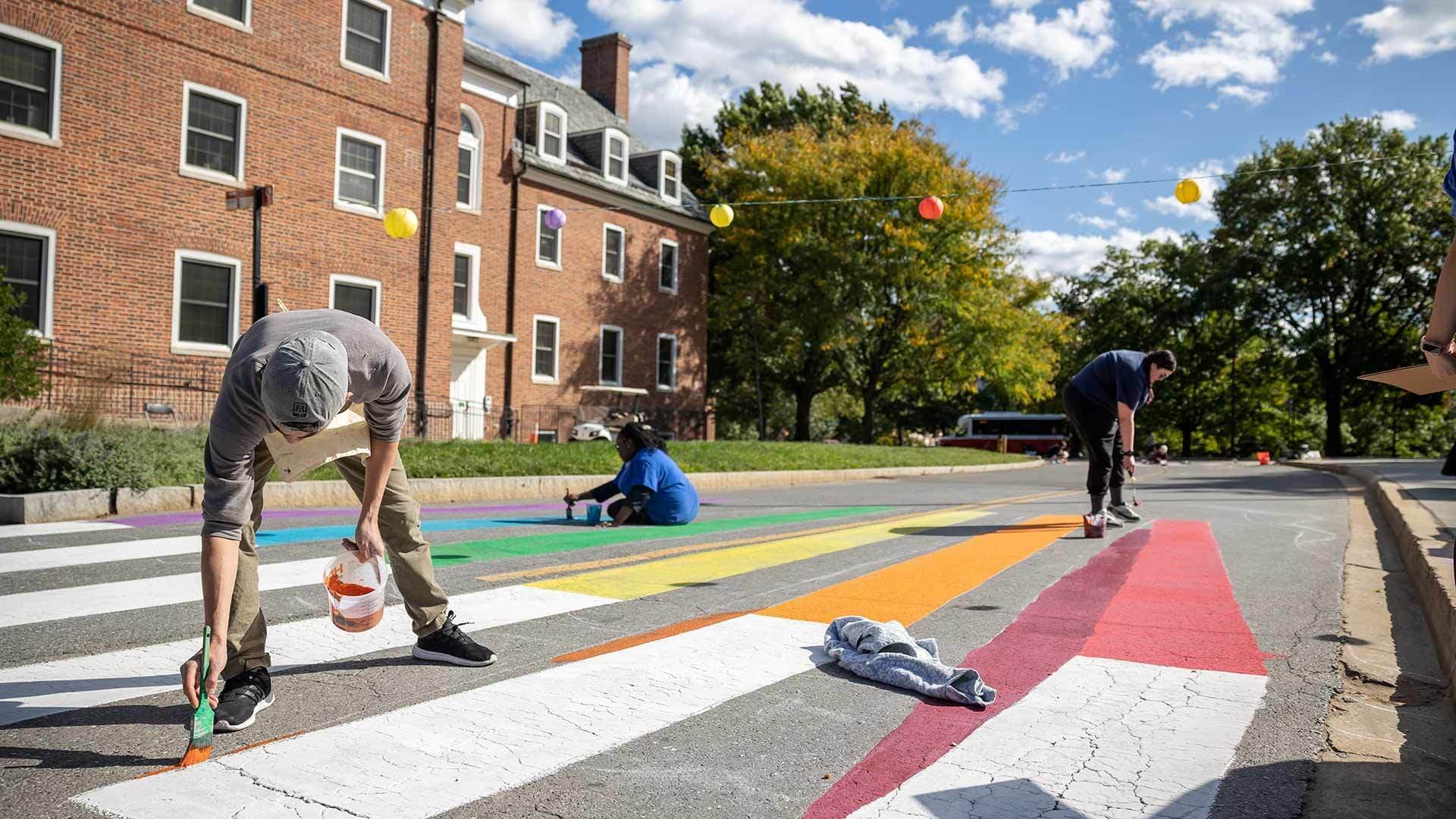 Painter applies colorful paint to a crosswalk near an academic building