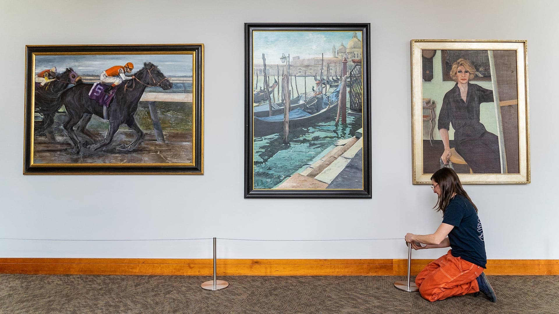 three paintings hang on wall as woman works in gallery