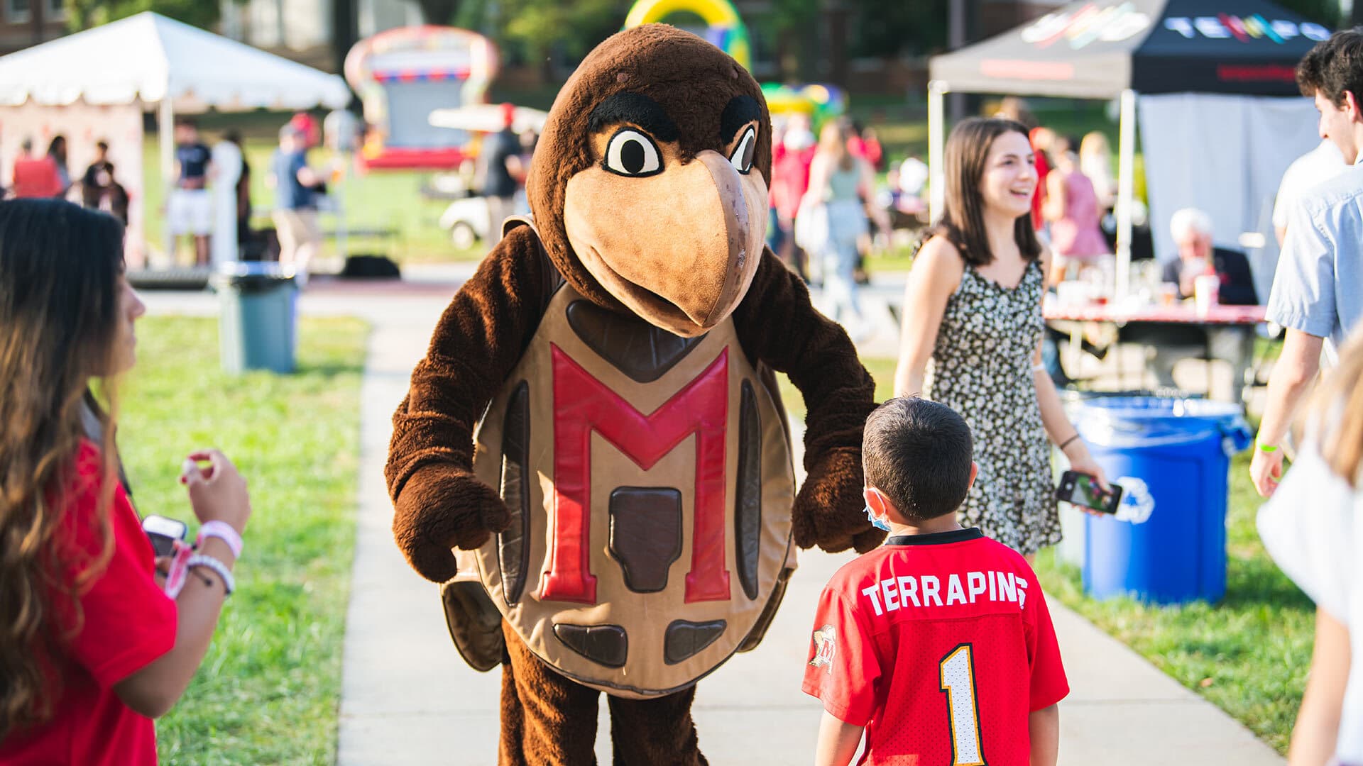 Testudo interacts with small child in UMD football jersey on McKeldin Mall