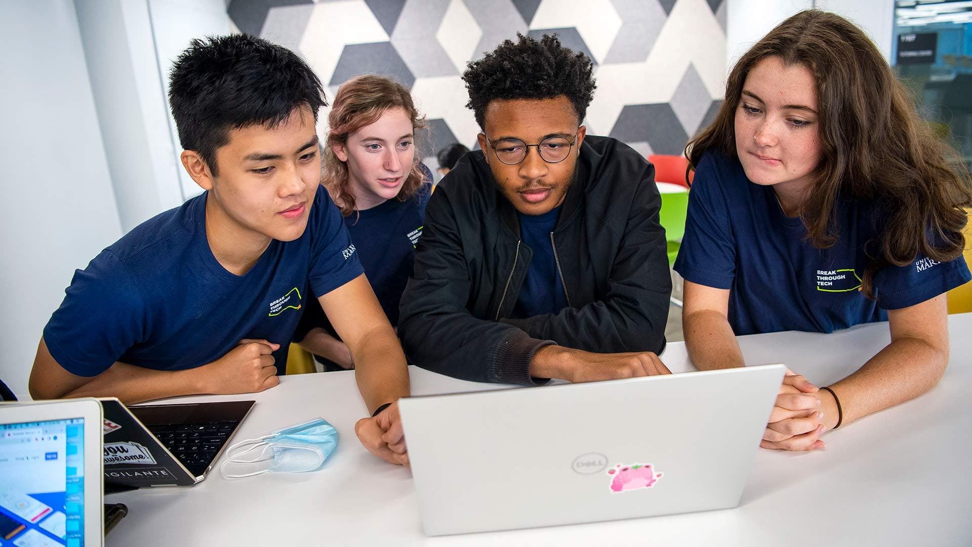 Four students huddle around a laptop