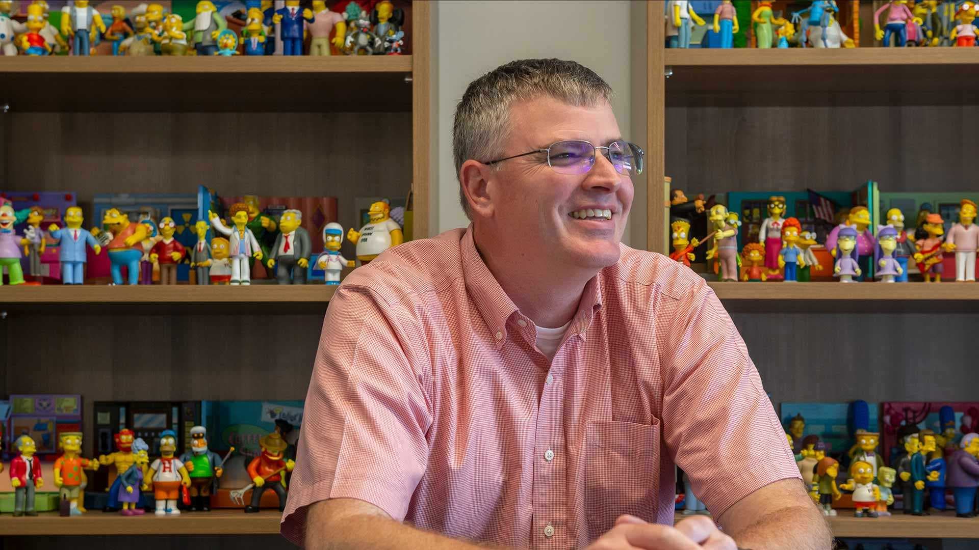 Derek Yarnell sits in front of shelves of Simpsons figurines