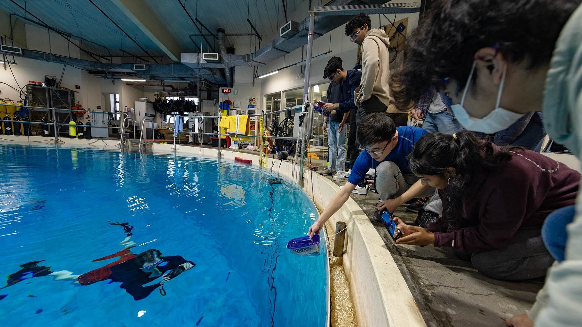 A person swims in a tank while students look on