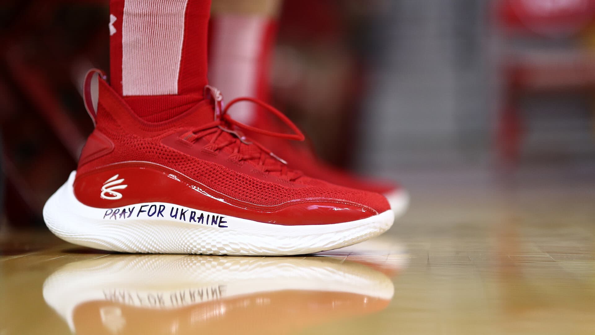 Red and white basketball shoe with "PRAY FOR UKRAINE" written on it in marker