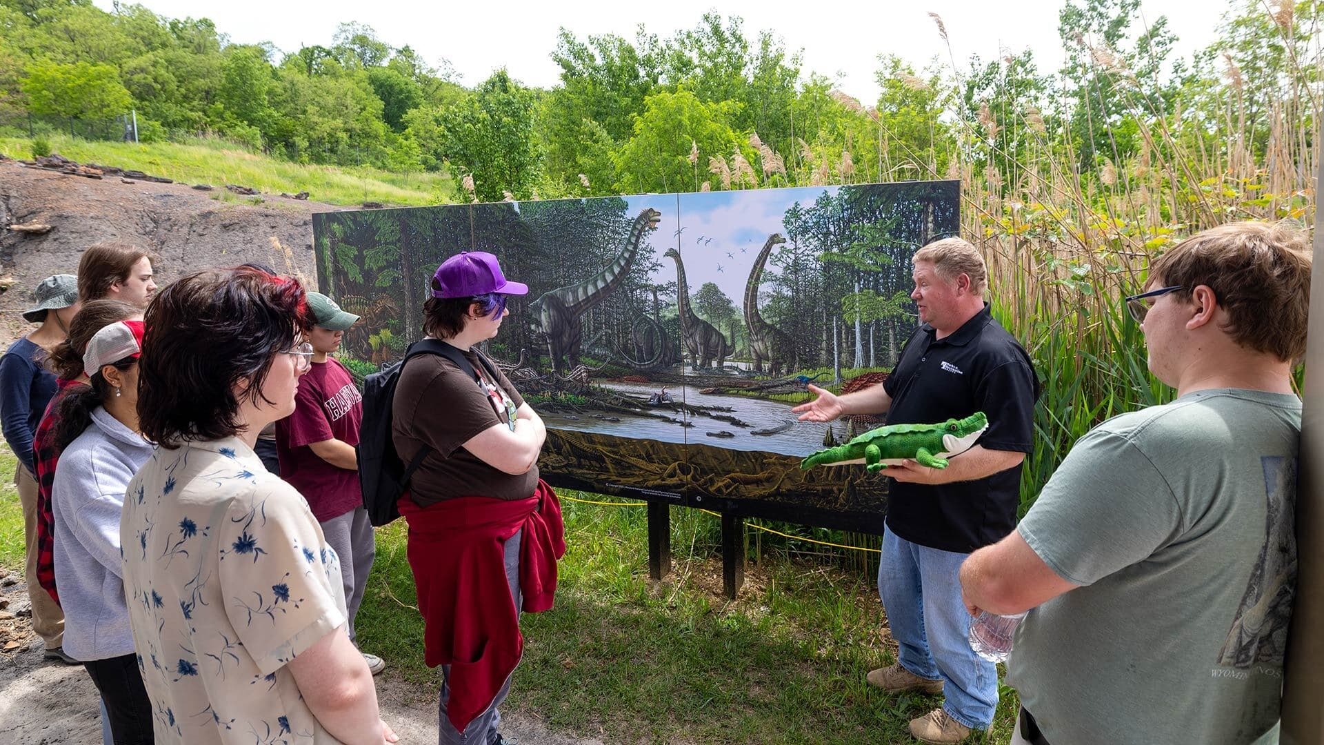 Students gather around as paleontologist John-Paul Hodnett stands in front of a rendering of dinosaurs in Maryland 115 million years ago