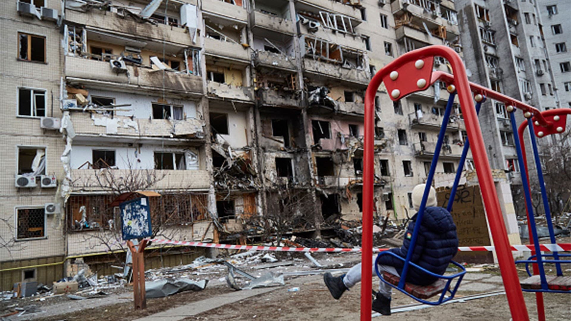 child on a swing outside a residential building damaged  by a missile