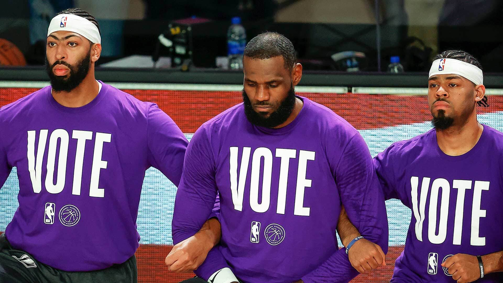 Basketball players linking arms while wearing purple jerseys that say "vote"
