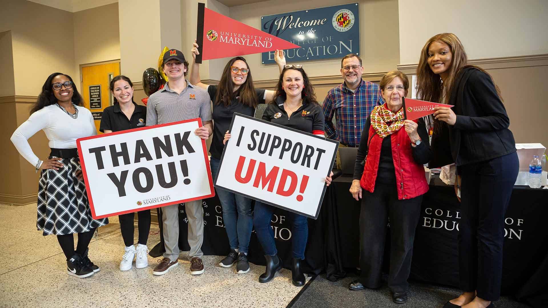 People hold "Thank you!" and "I support UMD!" signs and a UMD pennant