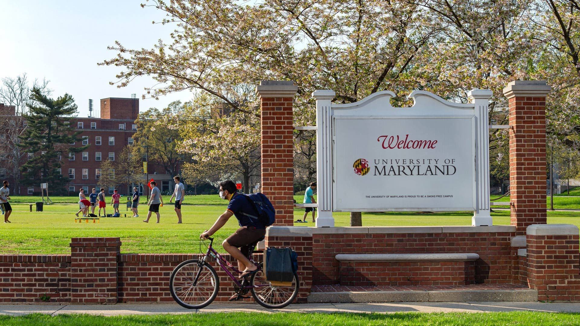 Student rides bike past "Welcome: University of Maryland" sign
