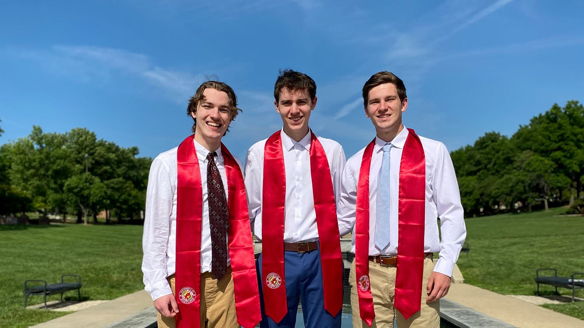 triplet brothers pose with red graduation sashes on McKeldin Mall
