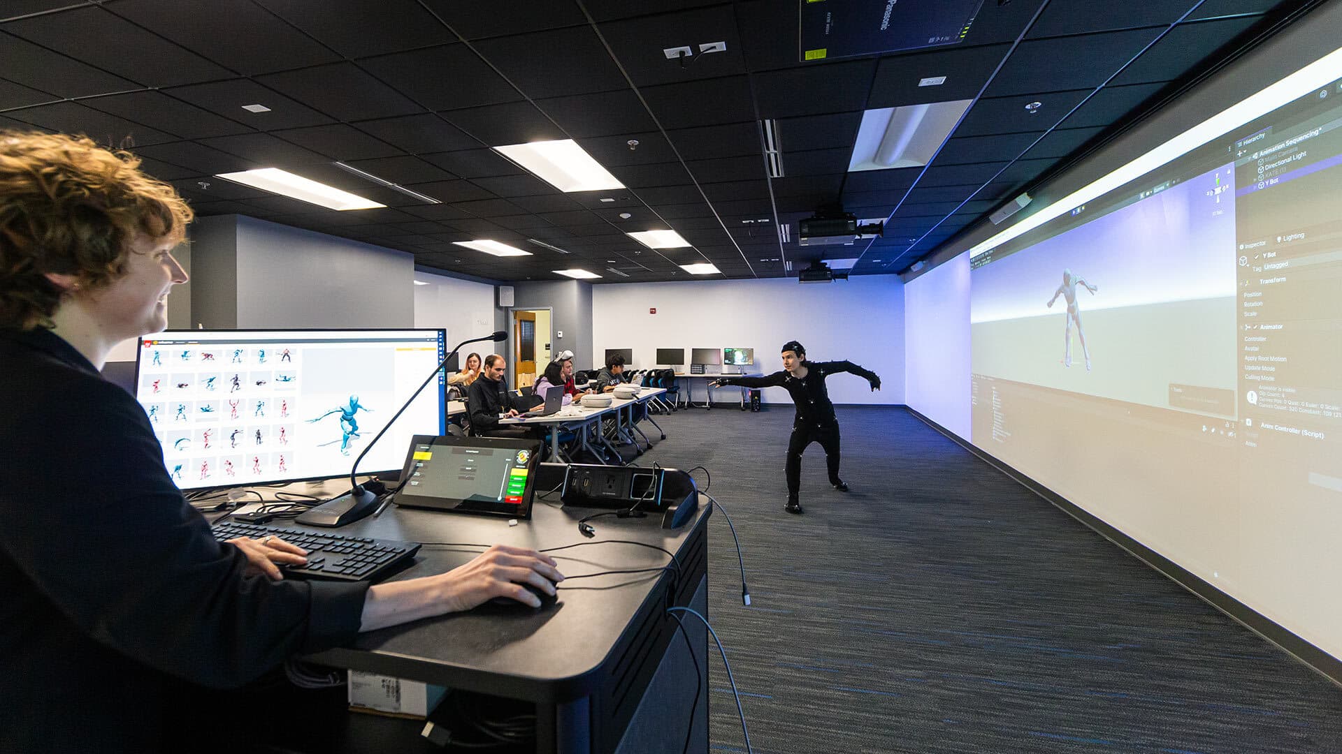 A woman operates a computer while a student in a motion-capture suit poses