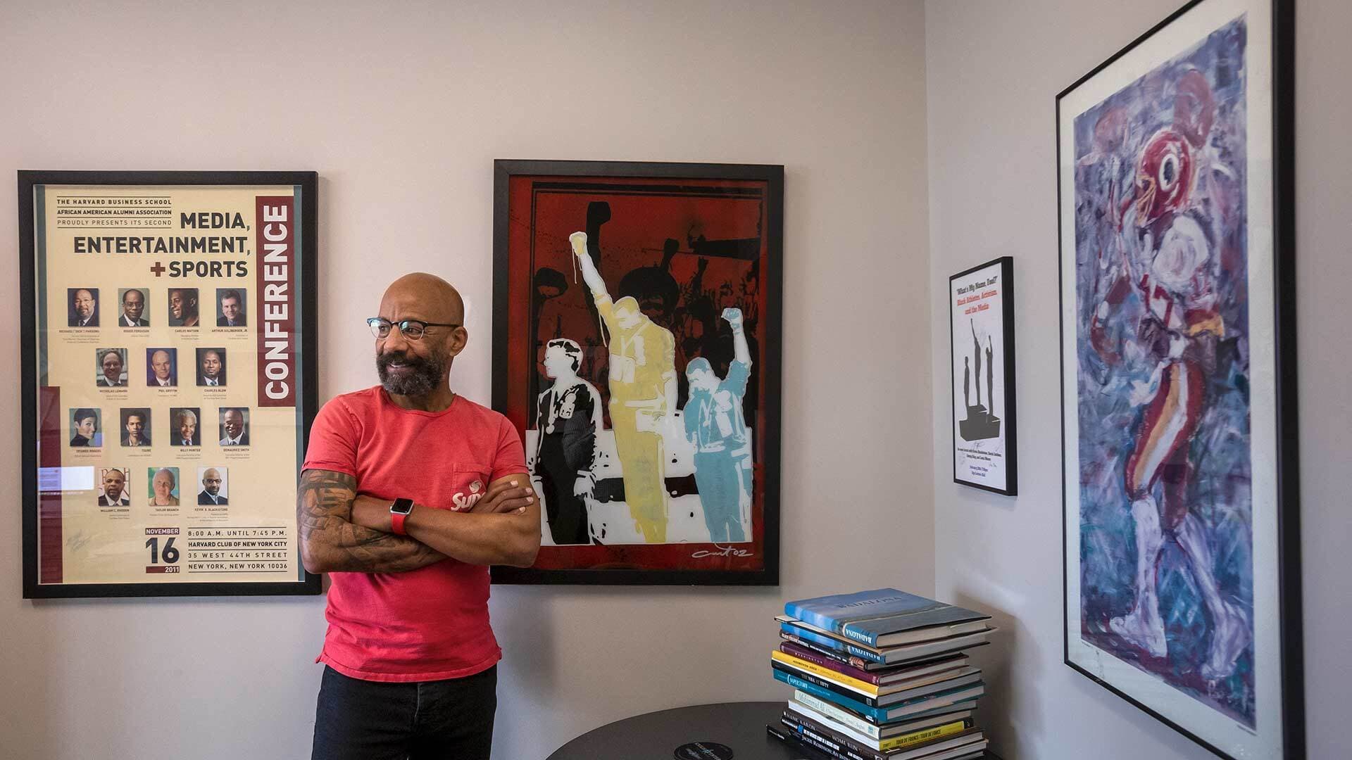 Kevin Blackistone stands in his office with Olympics Black Power salute artwork on wall