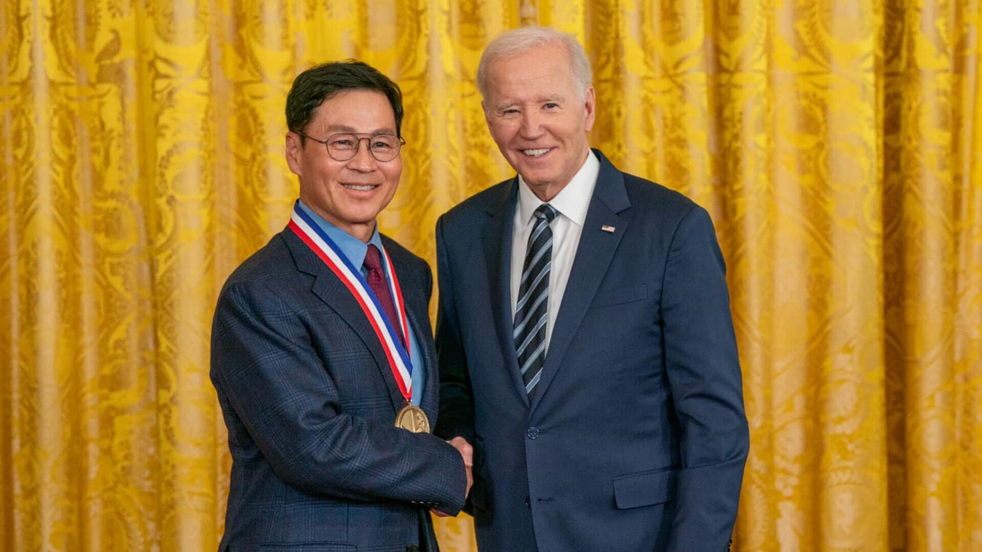 Jeong H. Kim with a medal around his neck, shaking hands with President Joe Biden