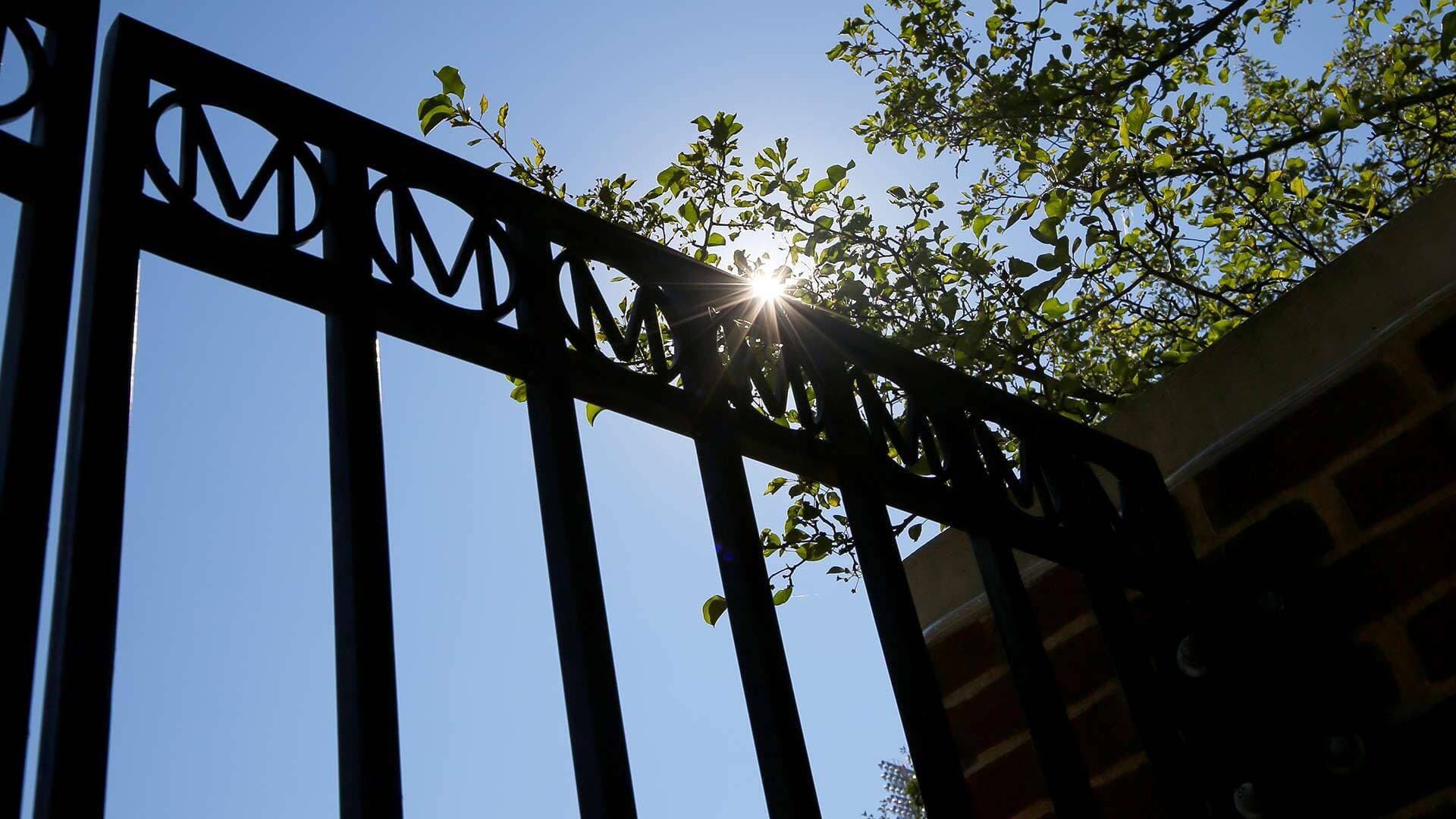 Sun shines through a black gate with M's at the top