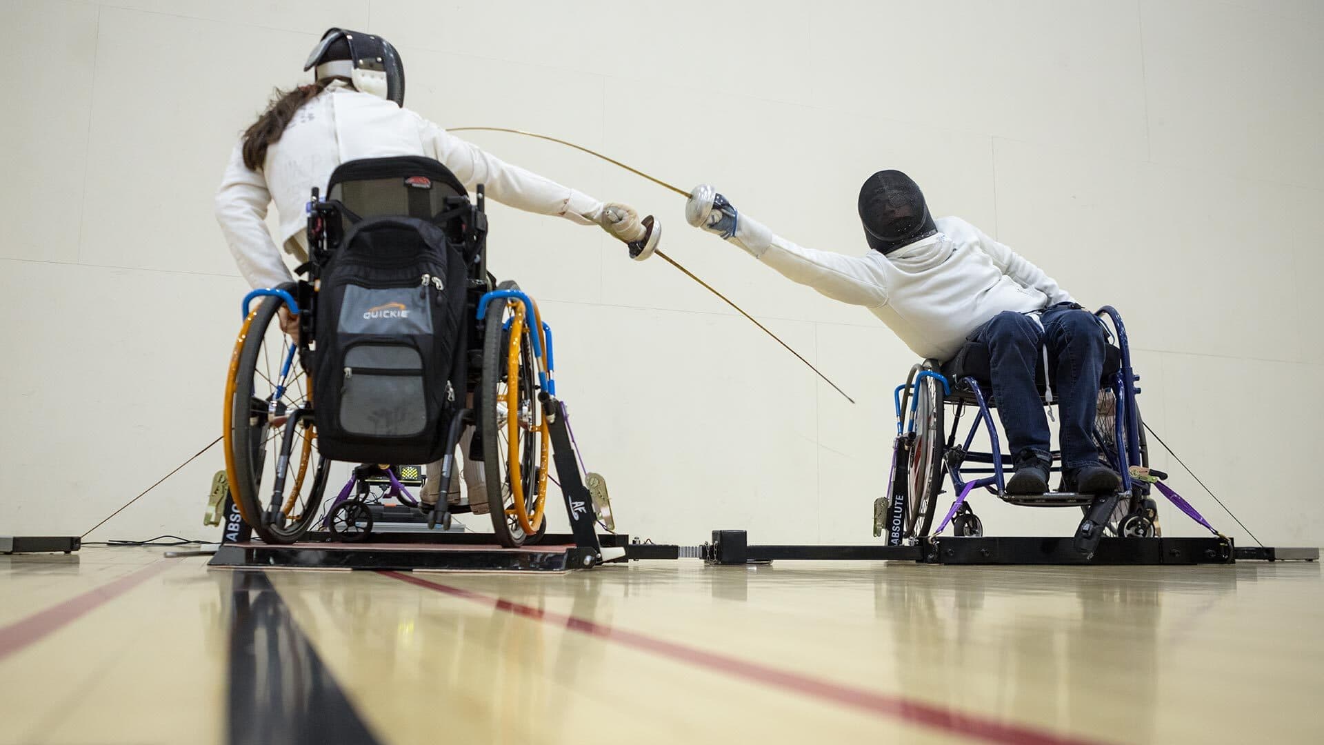 Two fencers in wheelchairs use accessible fencing frame