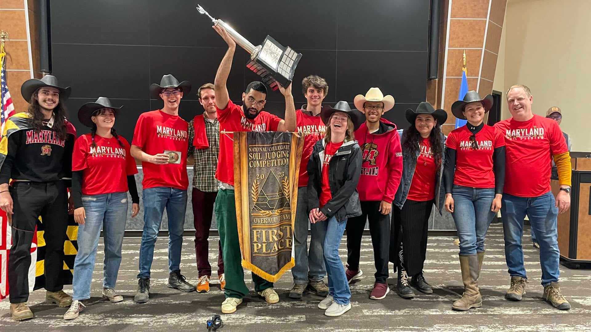 UMD soil judging team, wearing matching red Maryland T-shirts, hoists trophy