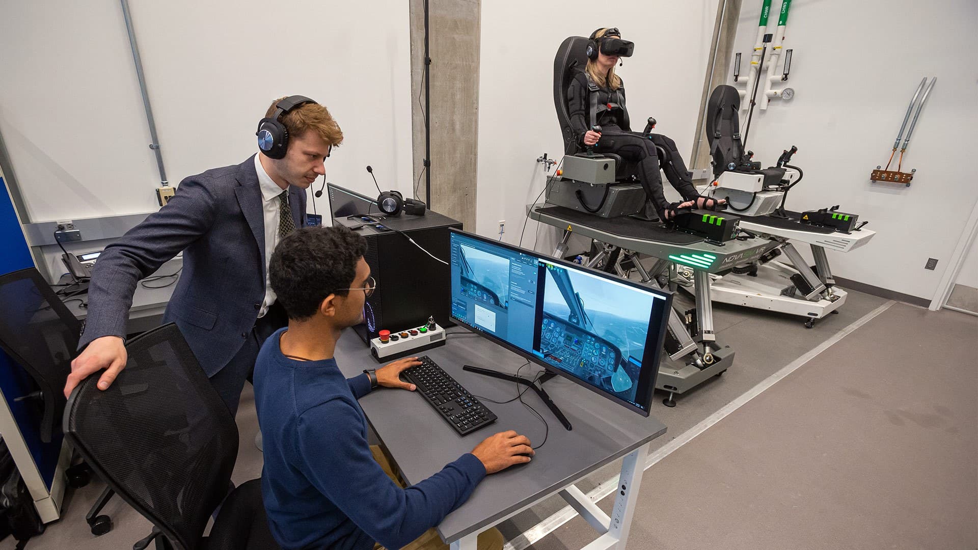 Two people view monitor while another sits in flight simulator chair