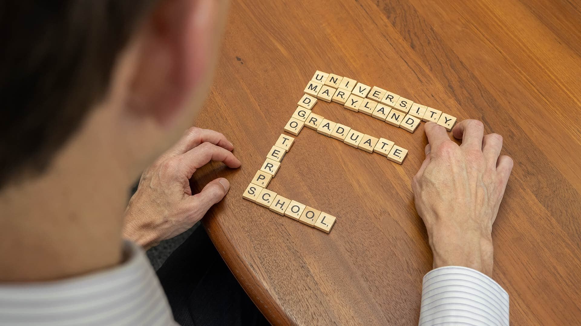 man creates acrostic on table with scrabble tiles