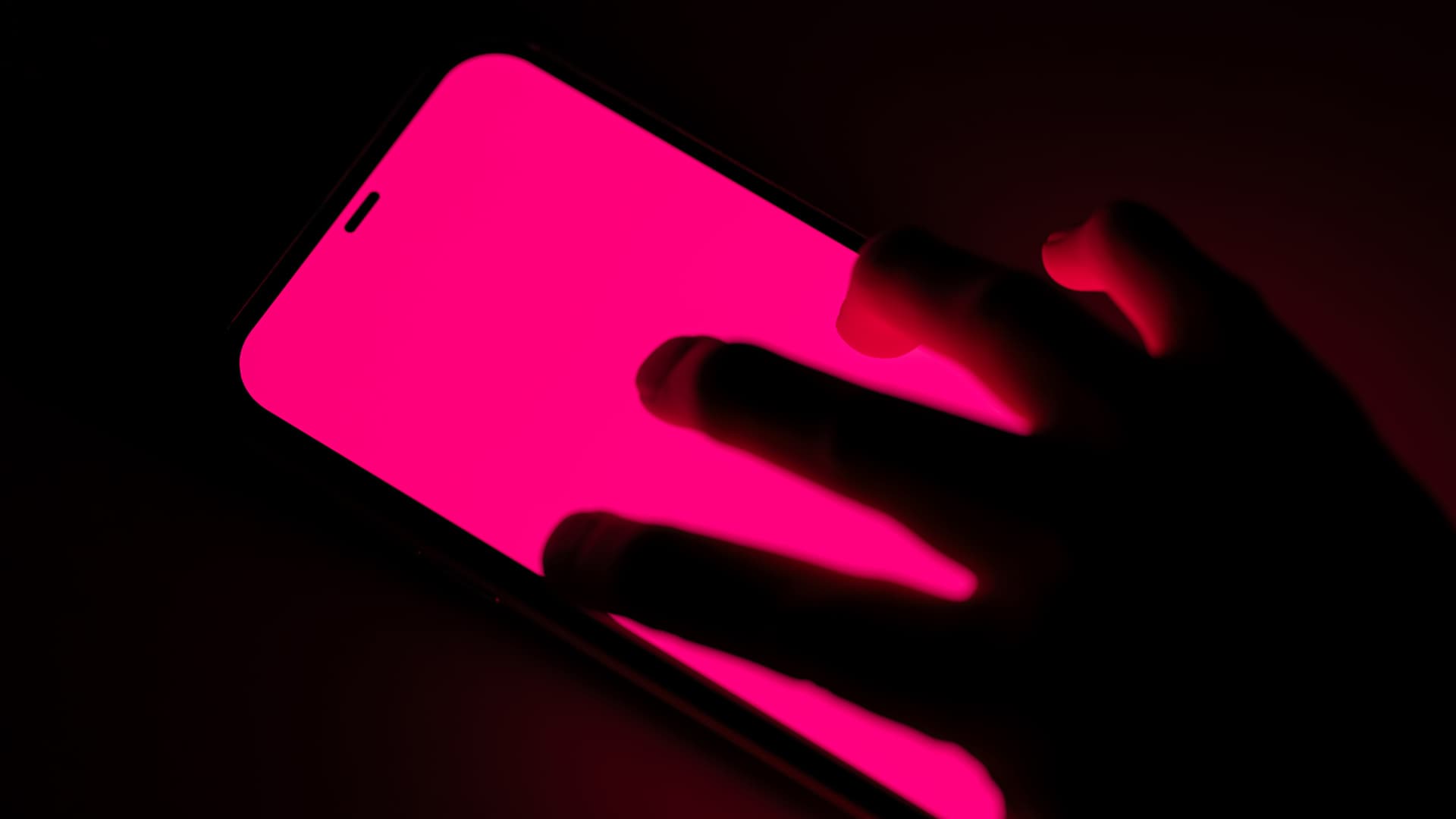 Eerie image of stalkerish looking hand on pink phone screen