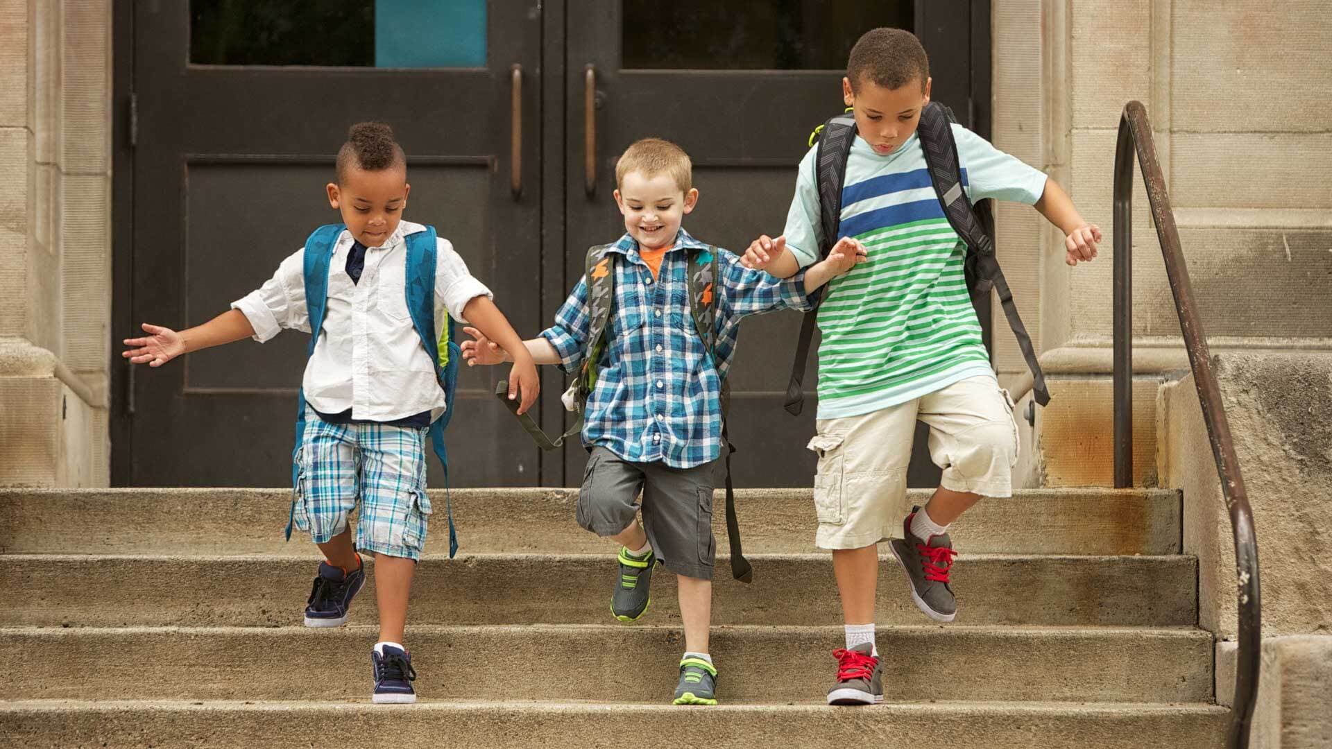 Three boys walk down the stairs of a school