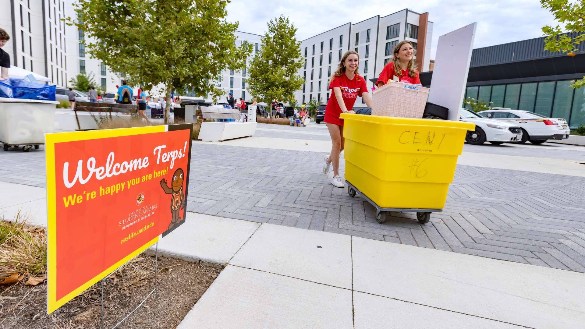 Two young women push a yellow moving cart