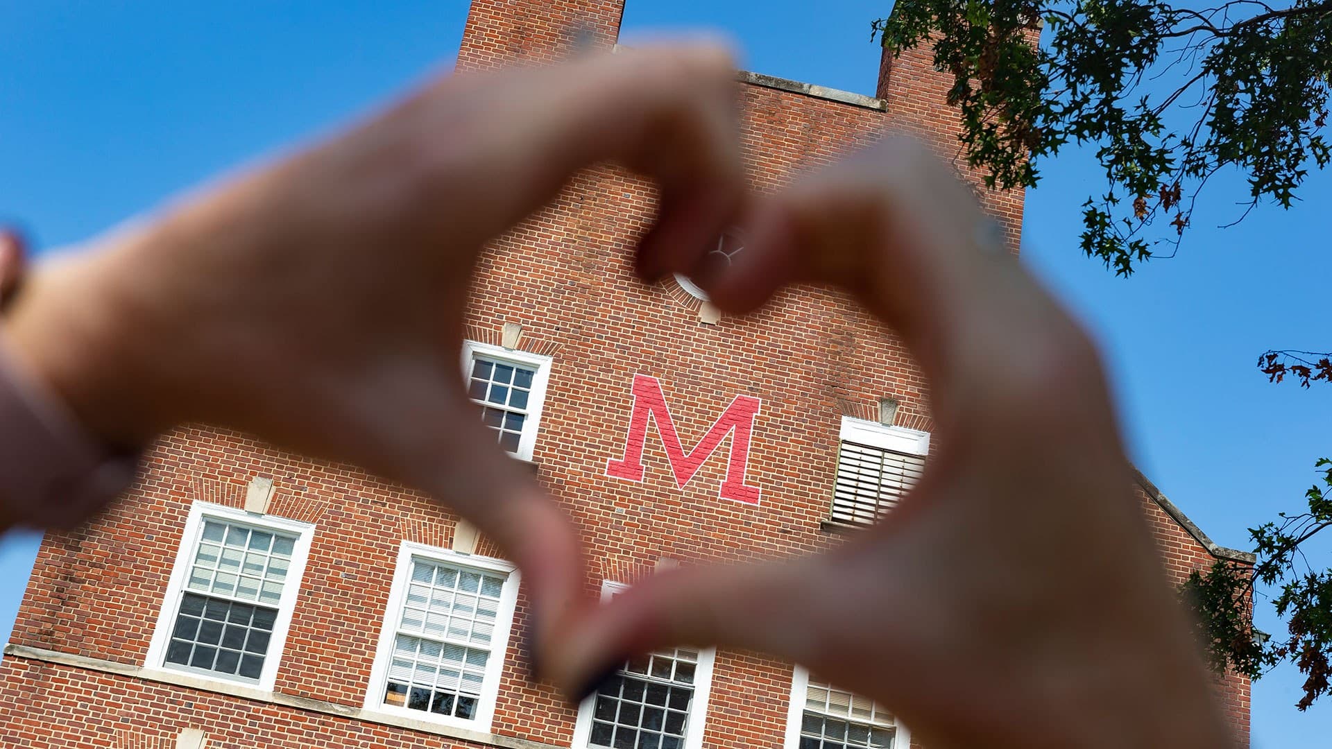 hands forming heart around red M on brick building