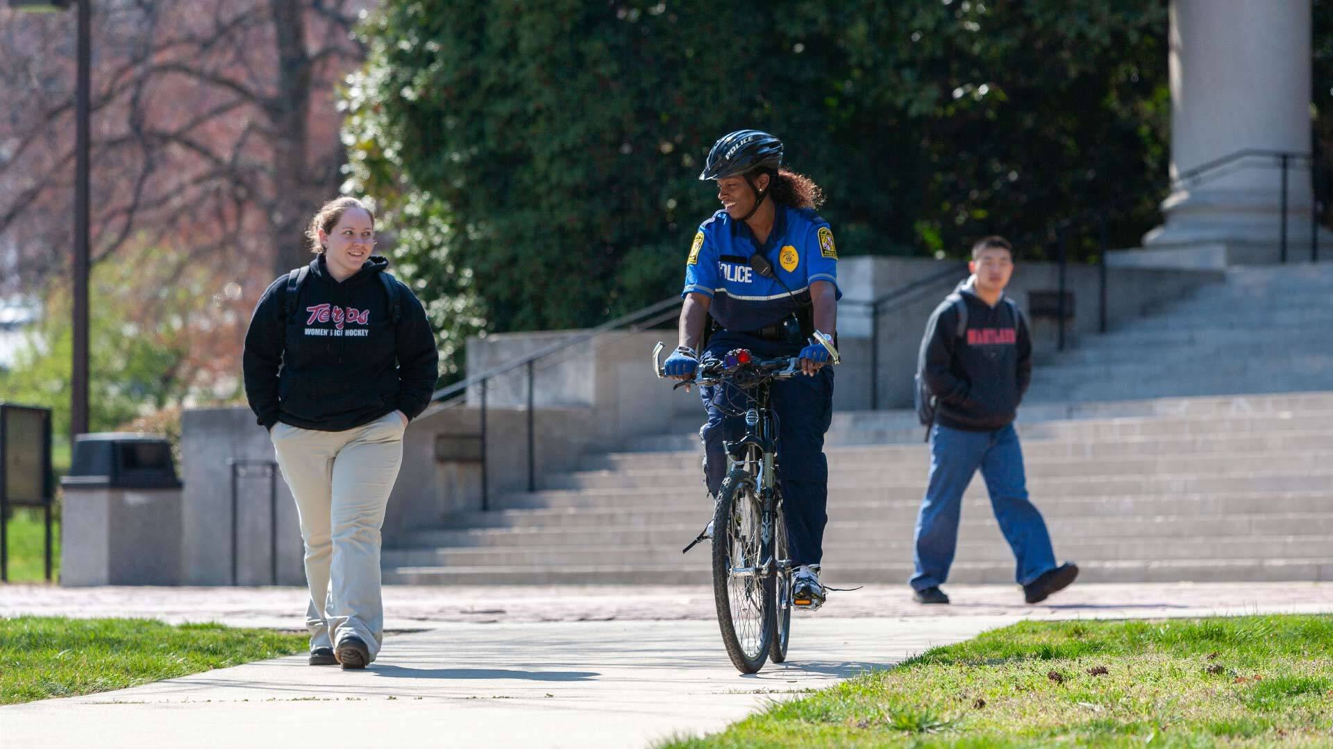 police officer rides bike past two students on campus