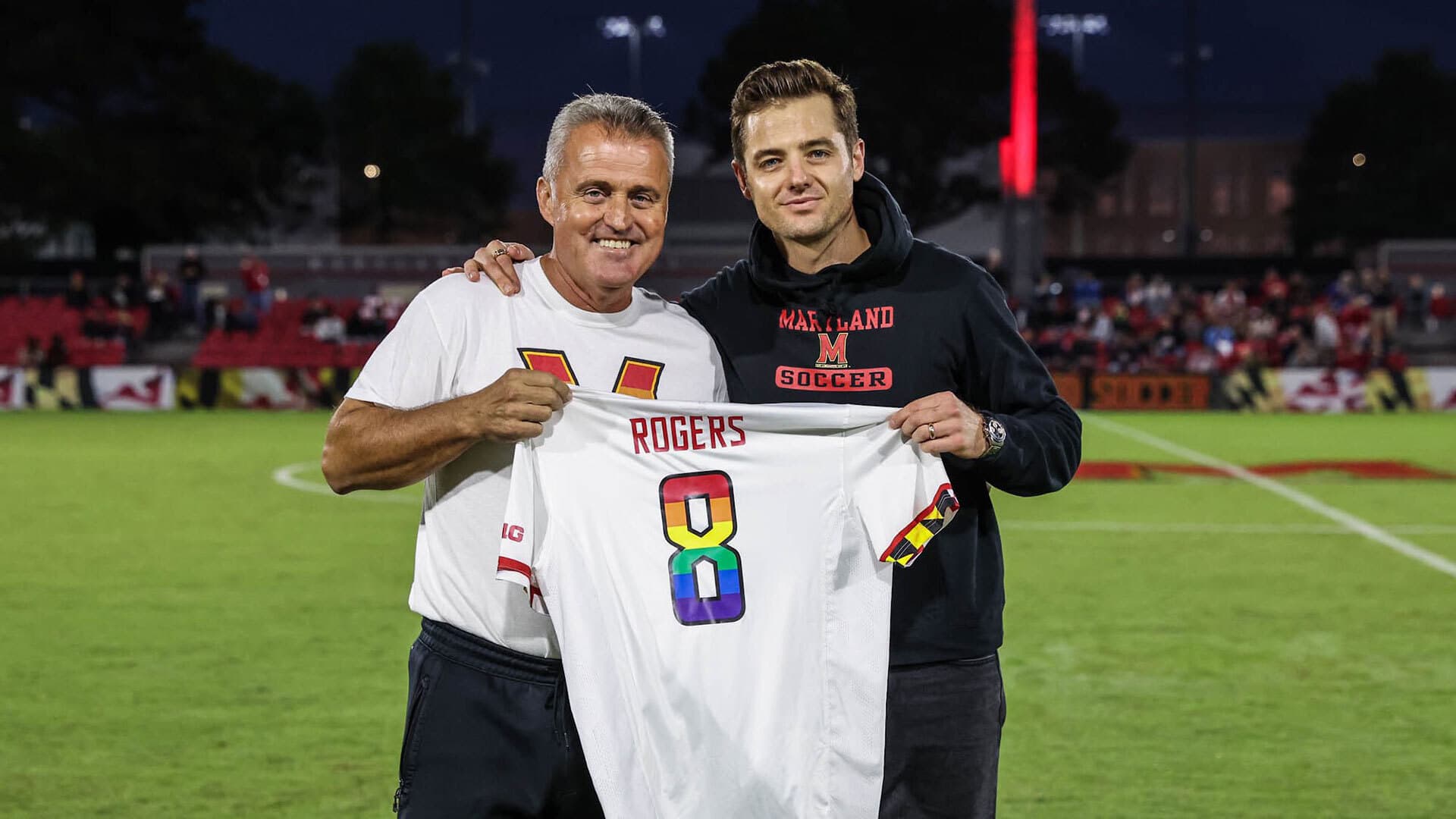 Sasho Cirovski and Robbie Rogers holding a white jersey that says "Rogers" with a rainbow number 8