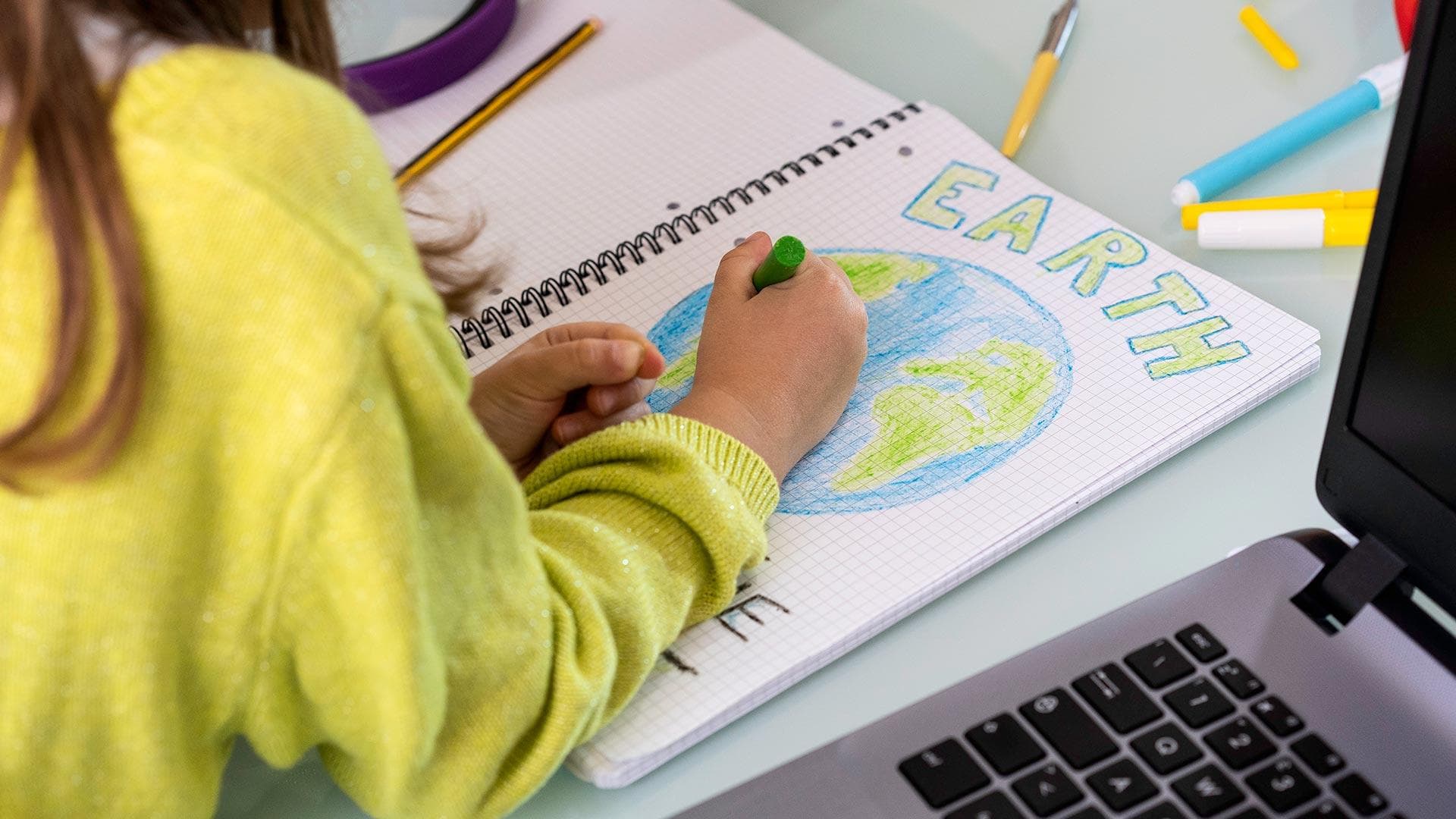 child draws EARTH in notebook