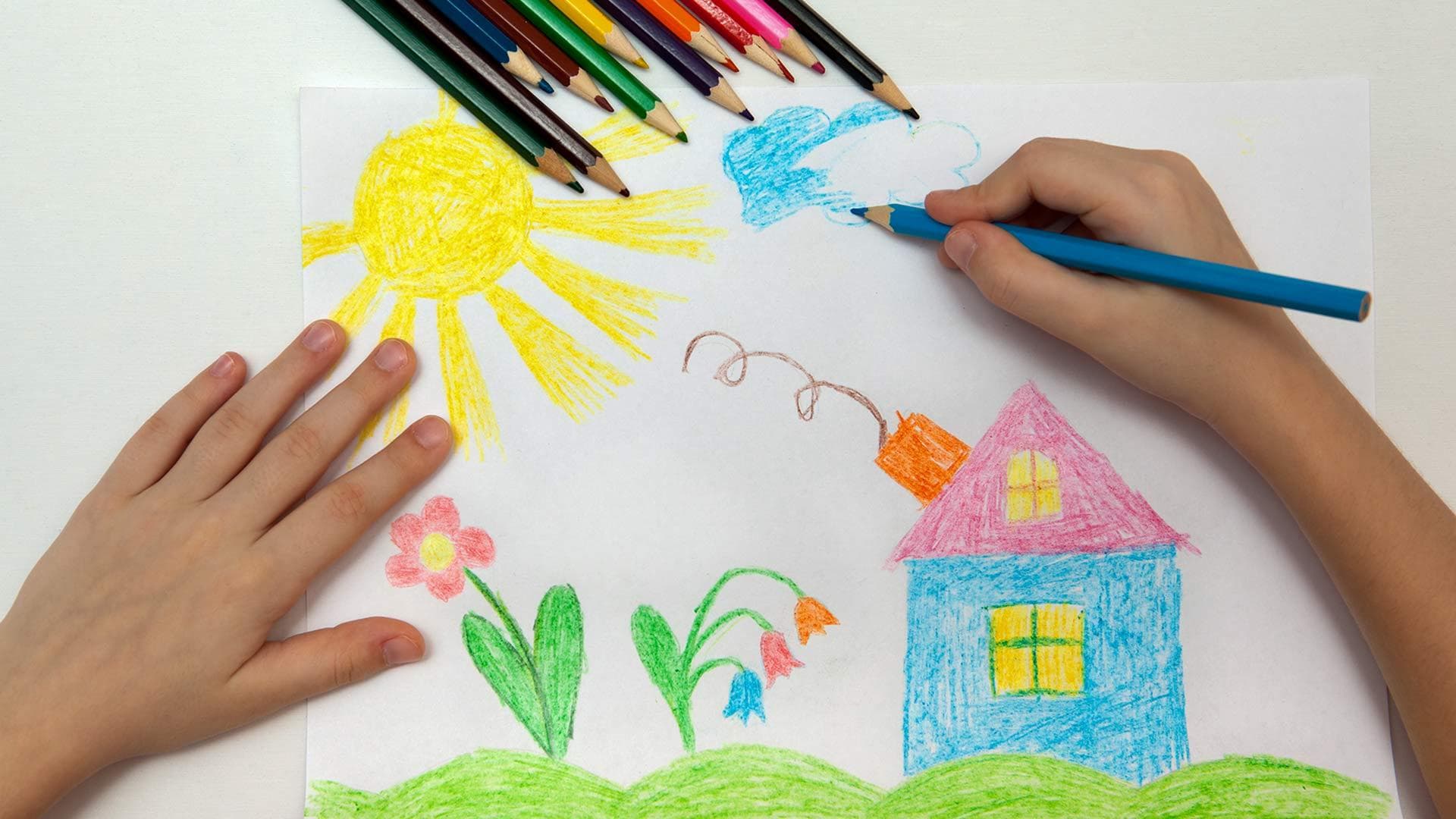 kid's hands drawing a house with colored pencils