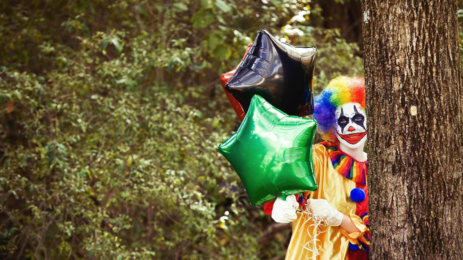A clown holding balloons in the woods
