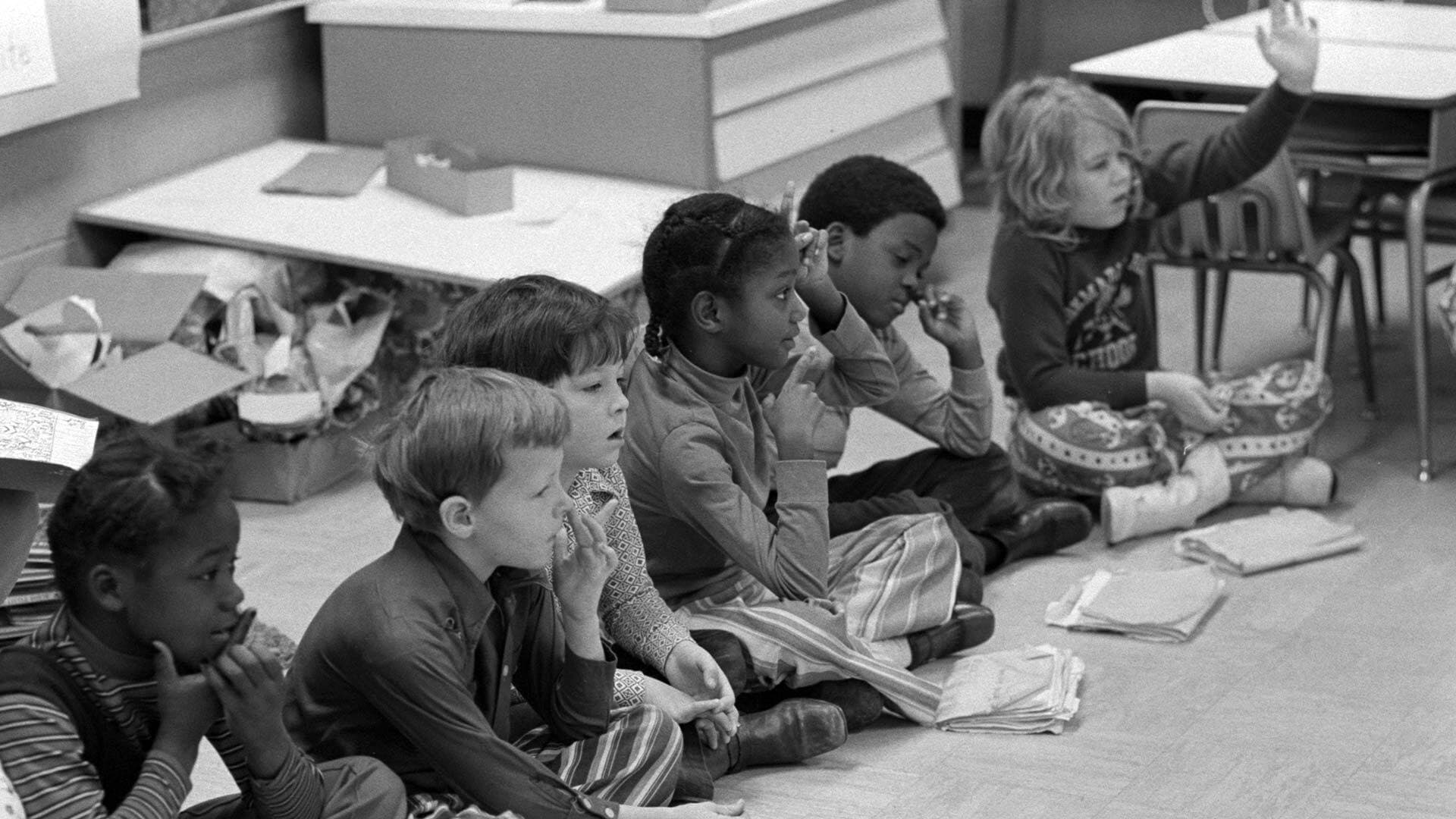 black and white children sit on the floor with papers