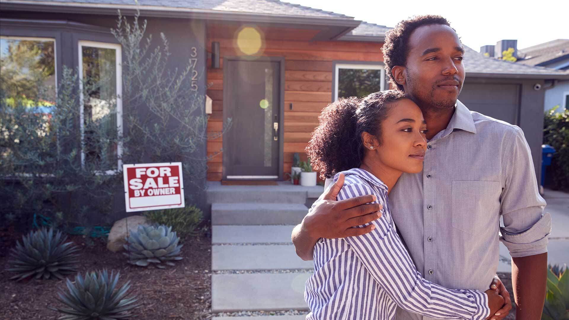 Couple in front of home with "for sale by owner" sign