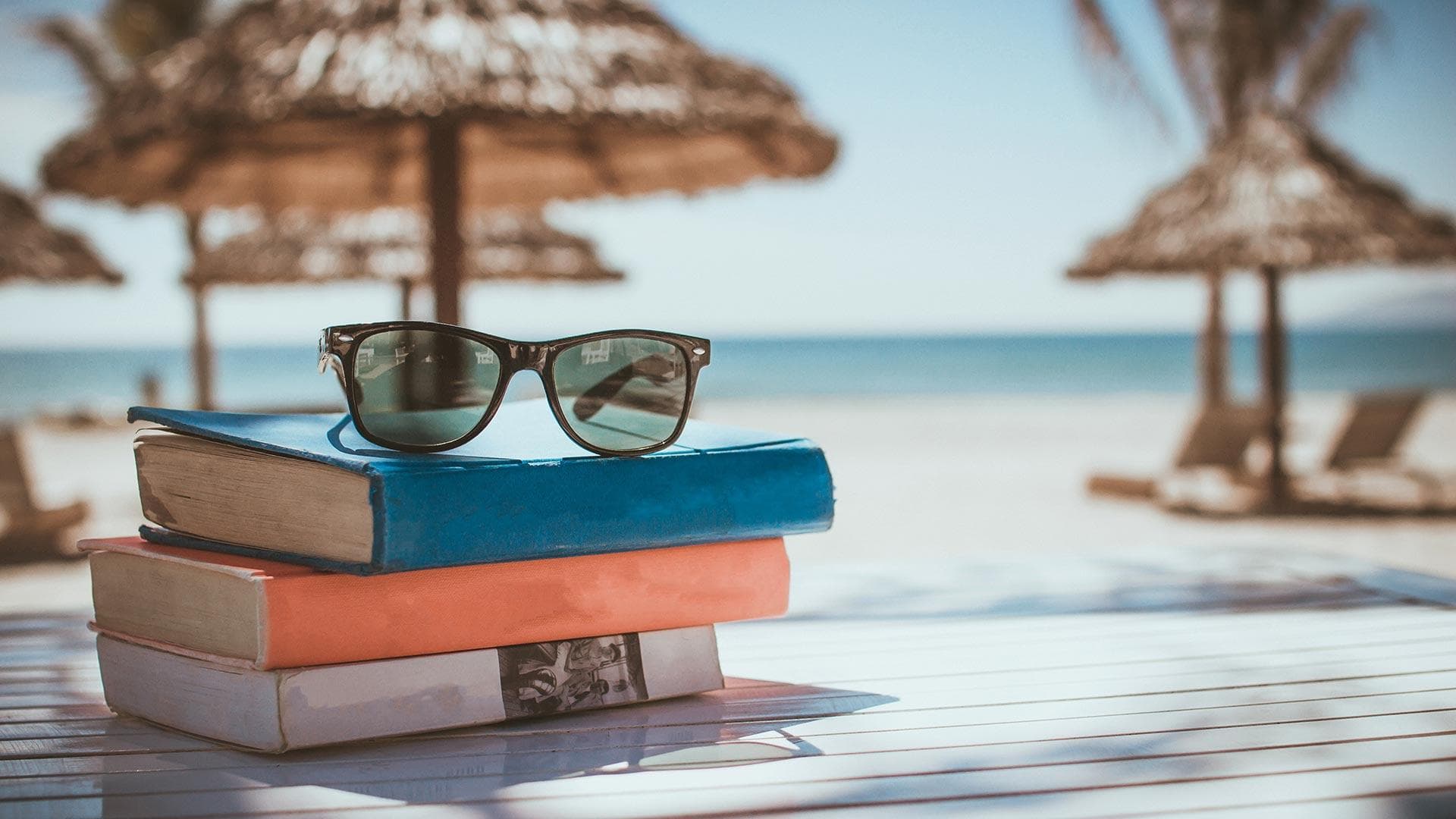 sunglasses on top of stack of three books at the beach